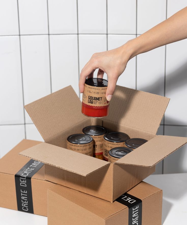 Mão retirando um pote de conserva de uma caixa de papelão pronta para envio